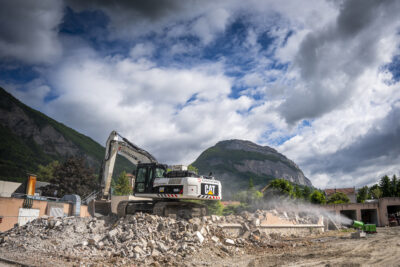 Une pelle mécanique opérant sur un tas de gravats, sur un chantier, avec de l'eau projetée. - Agrandir l'image 4 sur 9, fenêtre modale